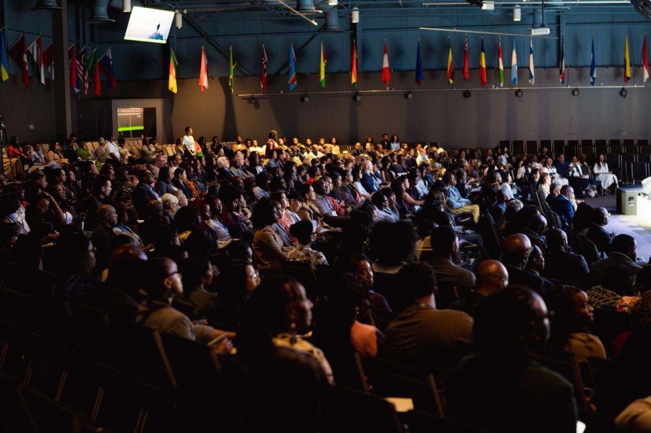 A full auditorium of attendees under a display of international flags at the GODfidence Conference