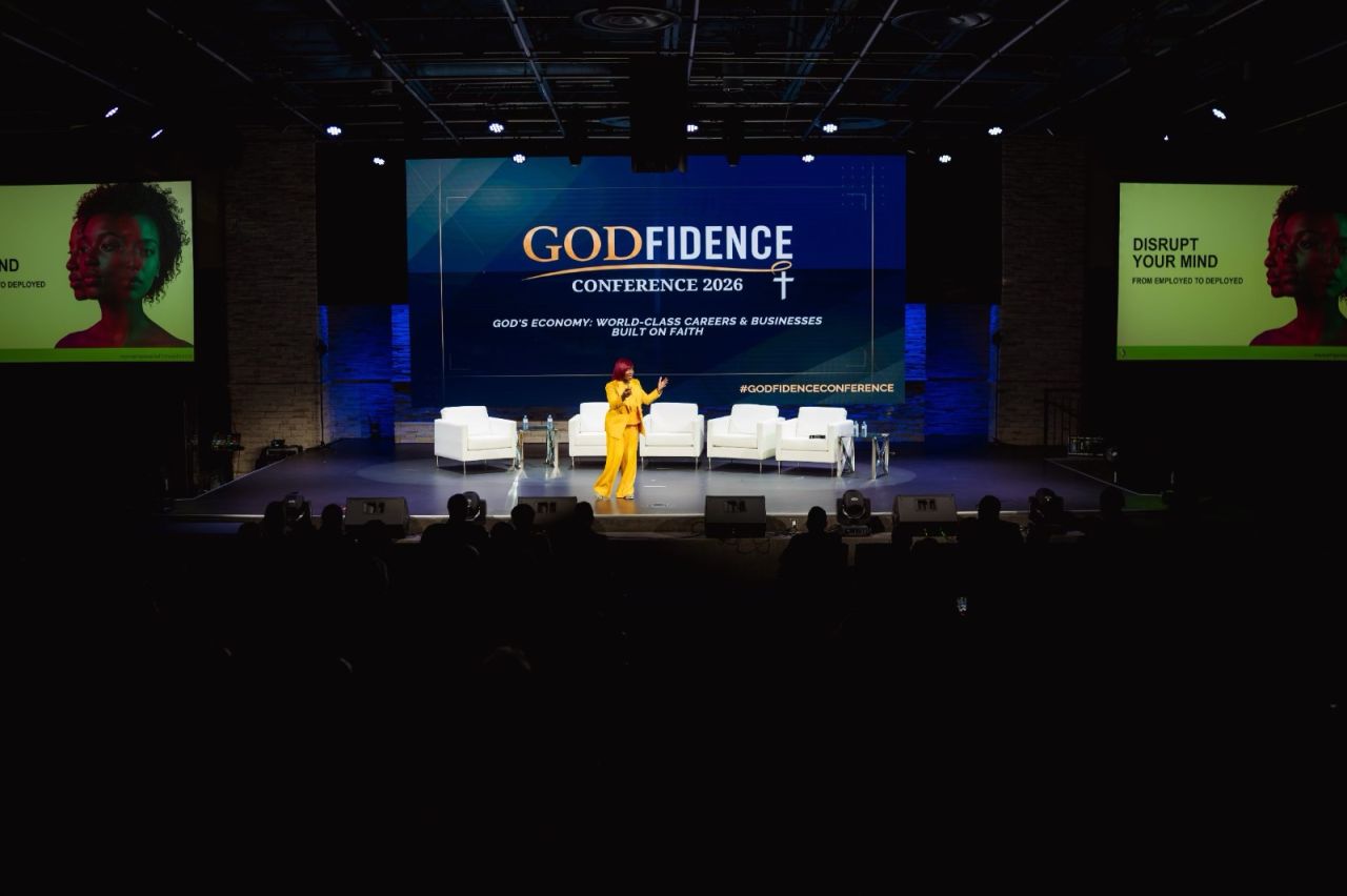 A speaker in a yellow suit addressing the audience from the GODfidence Conference stage