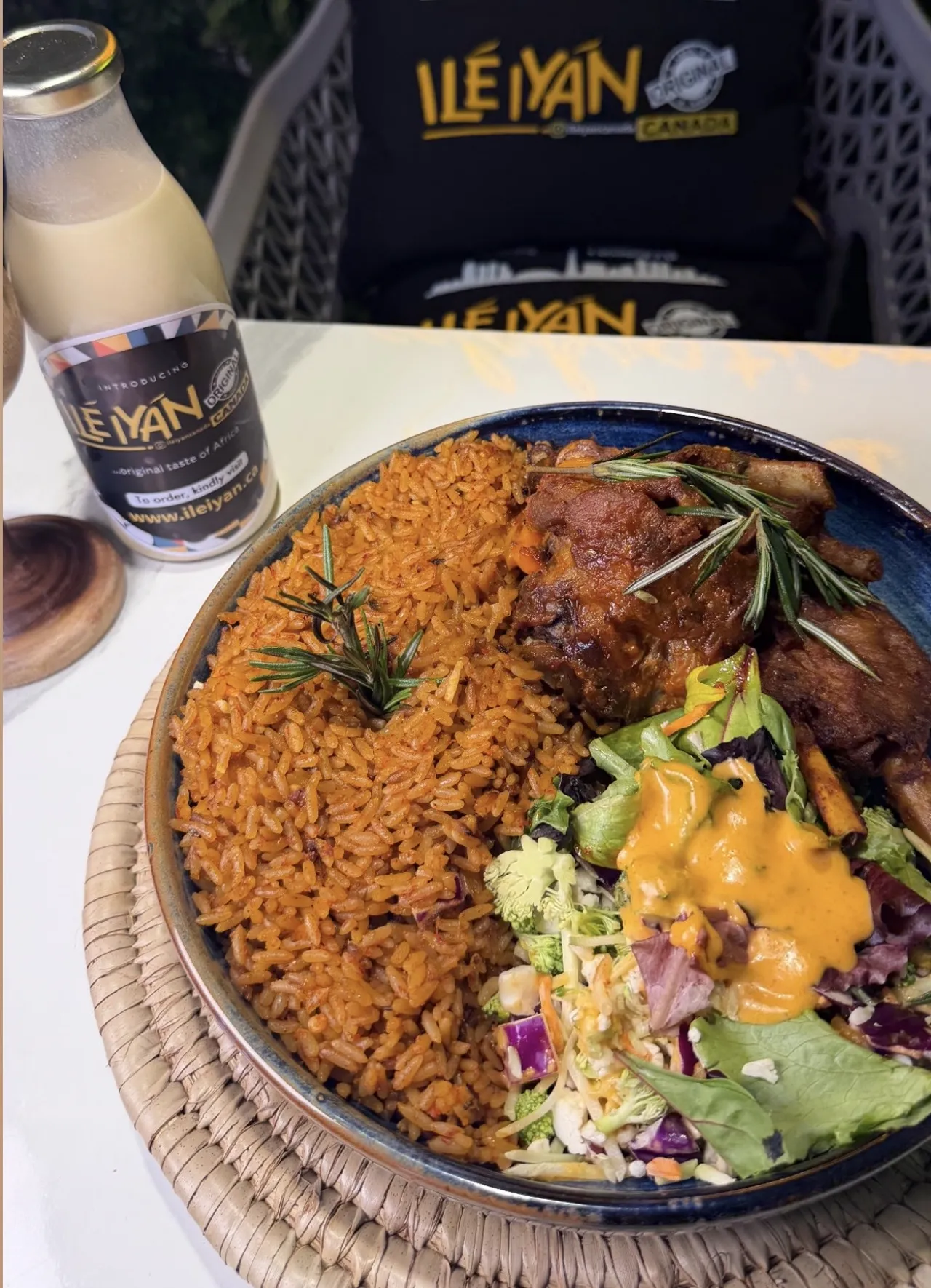 A plate of smoky party jollof rice with lamb chops and salad beside a bottle of Ilé Yàn's original taste of Africa drink