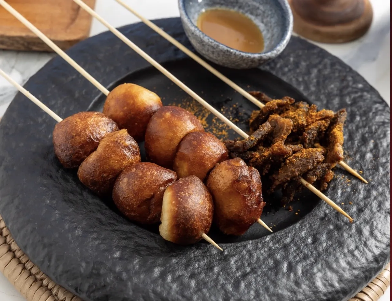 Golden puff puff on skewers with spiced suya on a black plate